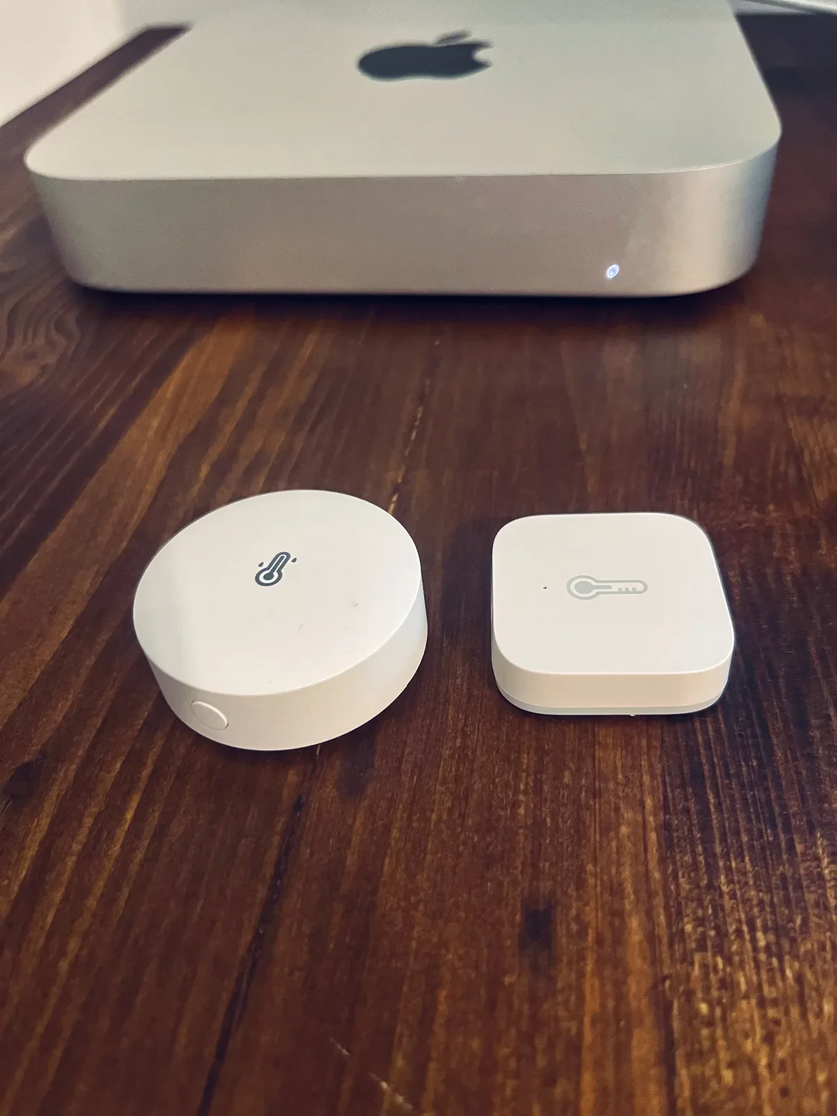 Due sensori di temperatura Zigbee su una scrivania in legno, usati come riferimento esterno per le valvole termostatiche